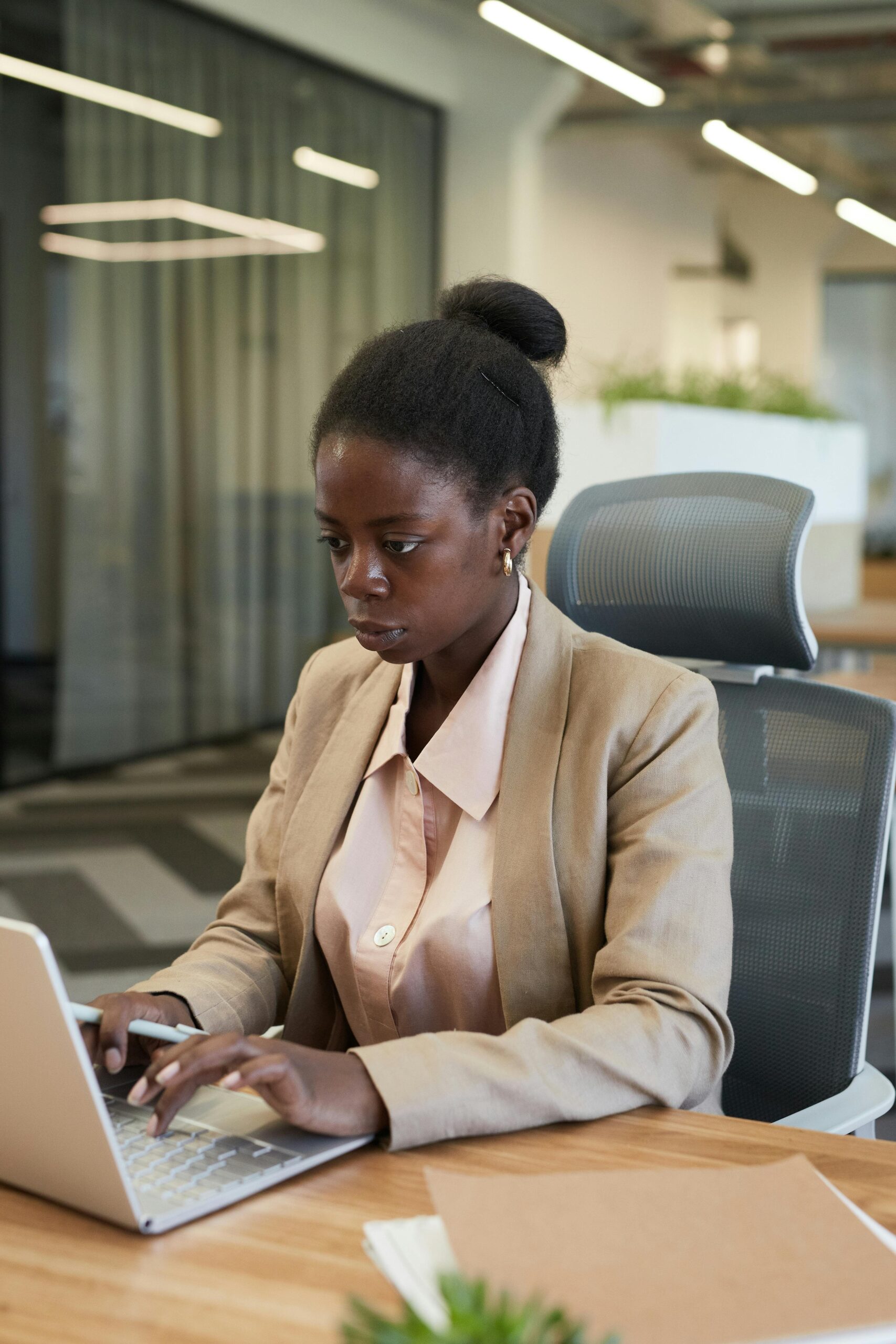 Professional woman in corporate attire works diligently on a laptop in a contemporary office setting.